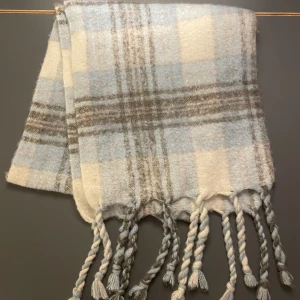 Stor halsduk i ljusa toner med fransar - Mysig halsduk till kyligare dagar 💕den har ett rutigt mönster i ljusblått, vitt och grått. Tjockt och fluffigt material med tvinnade fransar i ändan. Längden är 180cm och bredden 39cm. Använd ett fåtal gånger och inga defekter!