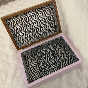 Smyckeskrin med zebramönster - Unikt smyckeskrin med trälock och lila målad botten. Insidan är fodrad med svartvitt zebramönster och har flera fack för att organisera ringar, halsband och armband. Perfekt för att hålla dina favoritsmycken snyggt samlade.