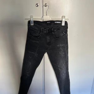 Replay Bronny svarta slim jeans 31 - Svarta Replay Bronny jeans med super slim fit och snygga slitningar framtill. Klassisk femficksmodell med coola detaljer på bakfickorna. Jeansen har en smal passform och är perfekta för dig som gillar en modern och stilren look.
