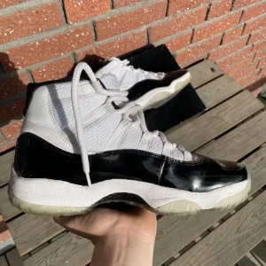 Nike Air Jordan 11 Concord Highs - Kvitto Finns! Nike Air Jordan 11 Concord med vit mesh och svart lackskinn runt hela skon. Snygga lila detaljer på yttersulan och klassisk Jumpman-logga på hälen. Skorna har snörning och en platt sula med rund tå. Perfekt för dig som vill sticka ut med en ikonisk sneaker.