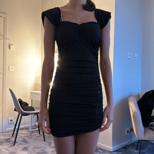 Svart kort klänning med puffärmar - Snygg svart klänning med kort längd och puffiga axlar. Klänningen har rynkade detaljer framtill och en tight passform som framhäver figuren. Axelpartiet är markerat och klänningen har en fyrkantig ringning. Perfekt för dig som gillar en stilren och trendig look.PERFEKT FÖR FESTER 🎉 