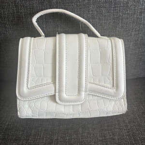 Axelväska  - Snygg vit axelväska med krokopräglat mönster och silverfärgad kedja. Väskan har både handtag och axelrem.