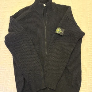 Stone Island stickad zip-tröja svart – storlek XL – helt ny - Snygg och klassisk svart stickad zip-tröja från Stone Island i storlek XL. Helt ny och aldrig använd – i perfekt skick.  ✔️ Mjuk och varm stickning ✔️ Dragkedja framtill ✔️ Ikonisk Stone Island-kompass på ärmen ✔️ Passar perfekt för höst och vinter  Färg: Svart Storlek: XL Skick: Ny / Oanvänd