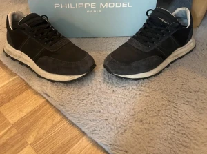 Svarta Philippe Model sneakers - Snygga svarta sneakers från Philippe Model med rund tå och platt sula. Skorna har snörning och är tillverkade i en mix av mocka och skinn, vilket ger en exklusiv känsla. Perfekta för dig som gillar stilrena och sportiga skor med en fransk touch.