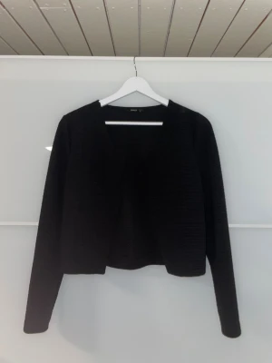 Svart ONLY Kofta - En svart kofta från ONLY i storlek S. Jackan har lång ärm, öppen framtill och är tillverkad i ett ribbat tyg som ger en snygg struktur. Enkel och stilren modell som är lätt att matcha med olika outfits✨  Den är jätteskön och behöver inte strykas:)