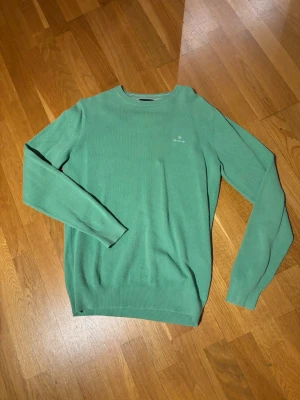 Grön stickad tröja från GANT - Snygg grön stickad tröja från GANT i storlek S. Tröjan har en diskret logga på bröstet och är tillverkad i mjuk bomull. Den har långärmad passform och ribbade muddar vid ärmslut och nederkant. Hör av dig vid minsta fundering!:)