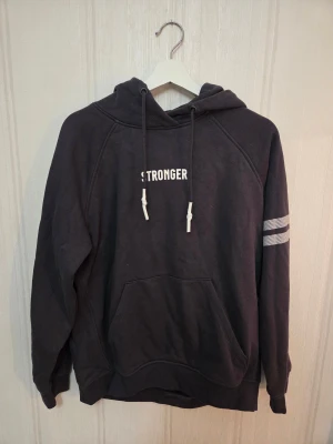 Mörkgrå hoodie från Stronger - Mörkgrå hoodie från Stronger med vit text på bröstet och två vita ränder på ena ärmen. Nypris är ca 700 säljes för 200. Djur finns i hemmet så lite katthår kan förekomma