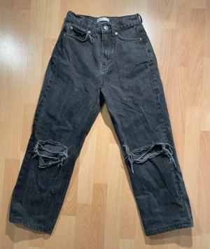 Svarta baggy jeans med hål från Gina Tricot - Svarta jeans med baggy passform och slitna hål över knäna. Wide legged med fem fickor.