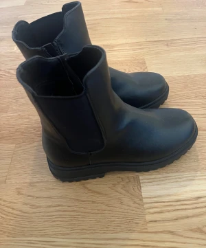 Svarta boots med dragkedja - Stilrena svarta boots i skinnimitation med grov sula och dragkedja på insidan. De har en rund tå och klassisk siluett som passar till många outfits. Perfekta för höst och vinter när du vill ha både stil och komfort.