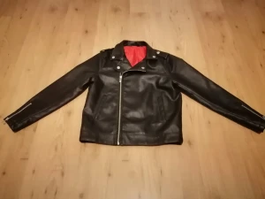 Svart skinnjacka med dragkedja - Snygg svart skinnjacka i klassisk bikerstil med silvriga dragkedjor och knappar. Jackan har röd insida, snedställd dragkedja framtill och detaljer vid axlarna. Pojke 10/11 år 