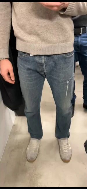 Levi's 501 blå jeans med slitning - Säljer ett par vintage Levi's 501 jeans i blå tvätt med snygga slitningar och en unik detalj med slits på höger ben. Rak passform, fem fickor och ikonisk röd Levi's-tag bak. W34 L30 passar dock mer som w31-33 L31-32 jag är 184cm lång och 81kg. Inga hål eller defekter som påverkar negativt, bara snygga slitningar! Priset är ej hugget i sten! Skickar ASAP!