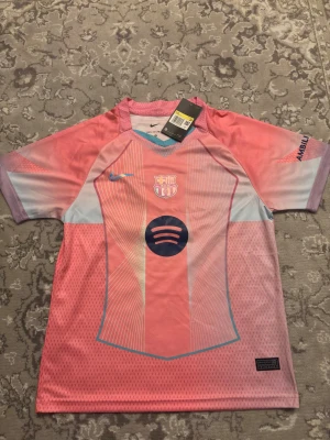 Barcelona 25/26 rosa specialutgåva  - Säljer en Barcelona fotbollströja med Lamine Yamal och nummer 10 på ryggen. Tröjan är rosa med ljusblå och vita detaljer, har korta ärmar och är tillverkad i lätt, ventilerande Dri-Fit material. Nike-logga och Barça-emblem på bröstet, samt Spotify sponsortryck.