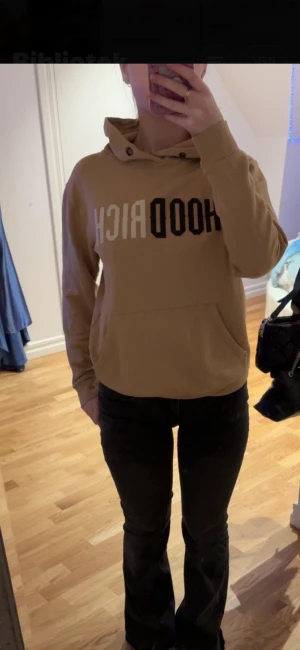 Beige hoodie med tryck från Hoodrich - Säljer en beige hoodie från Hoodrich med stort tryck i svart och vitt på bröstet. Tröjan har huva, känguruficka och långa ärmar. Perfekt för dig som gillar streetwear och vill ha en chill look. Passformen är normal och materialet känns som mjuk bomull.