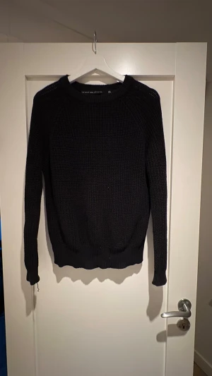Svart stickad tröja  - Svart stickad tröja från The Black Label Collection i storlek M. Tröjan har grovstickad struktur, rund hals och långa ärmar med ribbade muddar. Passformen är normal och den är perfekt för kyliga dagar. Enkel och stilren design som funkar till allt.