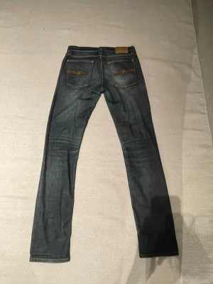 Nudie Jeans W28 L32 - Säljer ett par Nudie Jeans Tube Kelly i färgen Midnight Blue. De har klassisk femficksdesign, snygga orangea sömmar och Nudie-logga på bakfickan. Materialet är 98% bomull och 2% lycra för lite stretch. Passformen är rak och jeansen har en mörkblå tvätt.