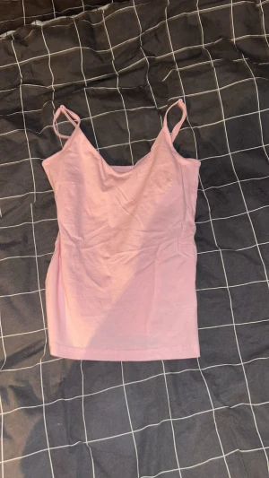 Ljusrosa linnetopp med smala axelband - Säljer en ljusrosa linnetopp med smala axelband och enkel design. Toppen är ärmlös och har en mjuk, rak passform som är perfekt för varma dagar. Materialet känns lätt och bekvämt mot huden.