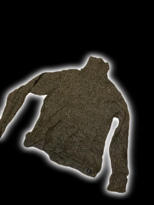 Brun stickad polotröja med lång ärm - Säljer en brunmelerad stickad polotröja från GANT med hög krage och långa ärmar. Tröjan har en mjuk och grovstickad känsla, perfekt för kyliga dagar. Diskret logotyp vid nederkanten. Passar dig som gillar klassisk och chill stil.