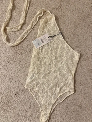 Spetsig vit ärmlös korsett-body - Säljer en vit korsett-topp i spets med snyggt mönster. Helt ny body med prislapp på. 