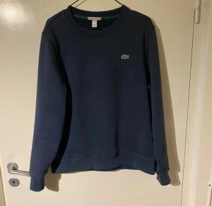 Mörkblå sweatshirt från Lacoste - Snygg mörkblå sweatshirt från Lacoste med klassisk krokodillogga på bröstet. Tröjan har rund hals, ribbade muddar och är tillverkad i mjuk bomull. Perfekt för dig som gillar stilrena och sportiga plagg.