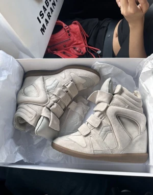 Beige Isabel Marant sneakers med plattform - Säljer ett par beige höga sneakers från Isabel Marant med plattformssula och rund tå. Skorna har flera kardborreband och är tillverkade i mjuk mocka med detaljer i skinn. Snygg chunky siluett som ger extra edge till din outfit. 