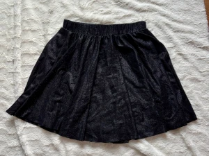 Svart glittrig kjol från VILA - Säljer en svart glittrig kjol från VILA i storlek M. Kjolen har en kort längd, elastisk midja och ett snyggt glittrande tyg som ger extra attityd. Materialet är mjukt och följsamt, perfekt för dig som gillar att sticka ut med din stil.