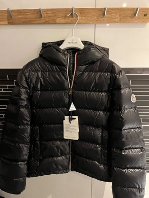 Moncler aubert jacka - Svart junior dunjacka från moncler, med allting og, alltså saker som väskan som jackan kom med (bild 5) och etiketterna och även moncler galjen. Jackan är köpt ifrån deras hemsida, jag är den enda ägaren av jackan. Om ni vill ha några mer bilder på jackan eller om ni har frågor osv så är det bara att skriva. Utropspris på 4000