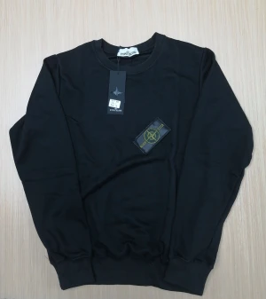 Svart sweatshirt från Stone Island - Svart långärmad sweatshirt från Stone Island med klassisk rund hals och ikonisk logopatch på vänster ärm. Tröjan har ribbade muddar vid ärmslut och nederkant, och är tillverkad i mjuk bomull som ger en skön och avslappnad passform.