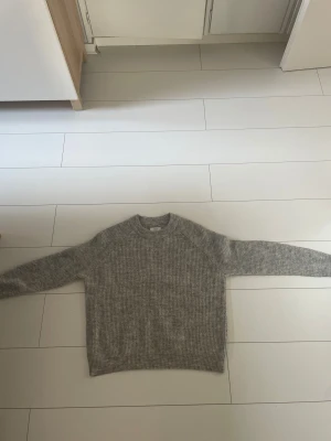 Grå stickad tröja från Envii - Mysig grå stickad tröja från Envii med ribbad struktur och rund hals. Tröjan har långärmade raglanärmar och är tillverkad i ett mjukt material som känns skönt mot huden. Perfekt för kyliga dagar, skriv ifall du vill ha en bättre bild på något speciellt☺️Använd fåtal gånger, kan upplevas som lite stickig 