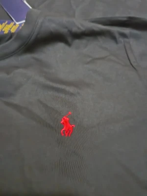 Svart t-shirt Polo Ralph Lauren - Svart t-shirt från Polo Ralph Lauren med röd broderad logga på bröstet. Modellen är slim fit och har rund halsringning och korta ärmar. Tillverkad i mjuk bomull för en skön känsla. Perfekt för en clean och stilren look.
