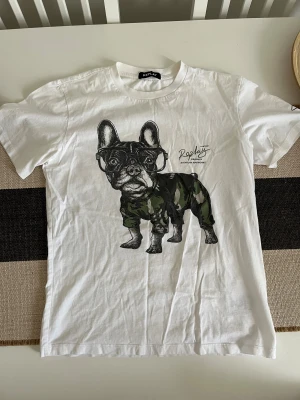 Vit Replay t-shirt med hundtryck - Vit t-shirt från Replay i bomull med coolt tryck av en fransk bulldog i glasögon och camouflagekläder. Klassisk passform och rund halsringning. Perfekt för dig som vill sticka ut med en unik och rolig print. Storlek S.