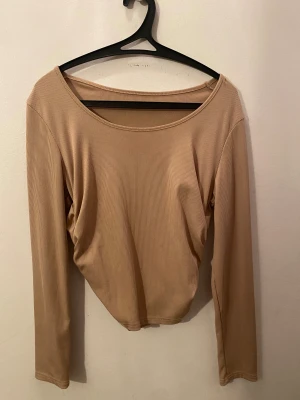 Beige ribbad långärmad topp - Säljer en beige långärmad topp med ribbad struktur och snygg rynkning på sidan. Toppen har en rundad halsringning och är figurnära i modellen. Perfekt att styla med jeans eller kjol för en chill look.