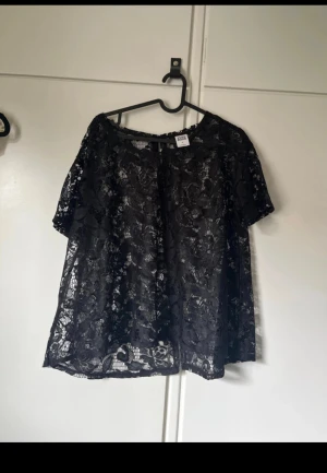 Svart spetsblus från Vero moda - Säljer en svart blus från Vero moda i genombruten spets med blommigt mönster. Blusen har korta ärmar och en lös passform, perfekt för dig som gillar en stilren men ändå romantisk look. Superfin att styla med jeans eller kjol.
