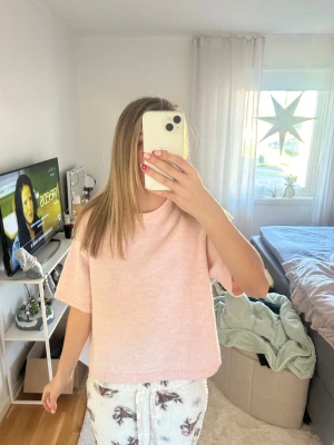 Ljusrosa stickad tröja med kort ärm - Supermjuk ljusrosa stickad tröja med korta ärmar och avslappnad passform. Tröjan har rund halsringning och ribbade kanter vid ärmslut och nederkant. Perfekt för lager-på-lager och chill dagar.