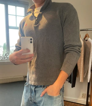 Grå half zip tröja Polo Ralph Lauren XL - Snygg grå långärmad tröja från Polo Ralph Lauren i storlek Barn XL, passar från 160-170 perfekt. Tröjan har en klassisk half zip-dragkedja, ribbade muddar och röd broderad logga på bröstet. Perfekt till jeans för en clean och chill look.