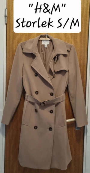 Beige trenchcoat från H&M S/M - Snygg beige trenchcoat från H&M i storlek S/M. Jackan har klassisk dubbelknäppning, krage och bälte i midjan för en stilren look. Perfekt för dig som gillar tidlös design och vill ha en jacka som funkar till många outfits.