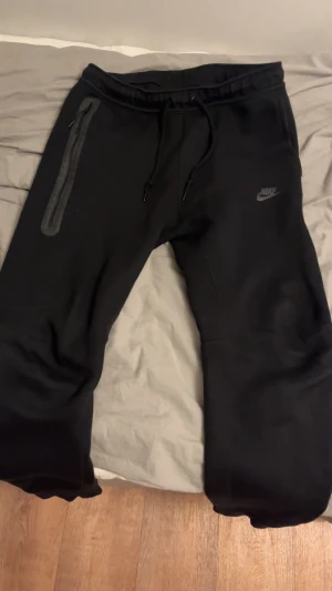 Svarta Nike tech fleece byxor använda 2 gånger  - Svarta mjukisbyxor från Nike med dragsko i midjan och en snygg dragkedjeficka på sidan. Byxorna har en diskret Nike-logga på låret och är tillverkade i mjukt material som är perfekt för chill eller träning. Knappt använda kan gå ner i pris vid snabbköp inga skambud!!!