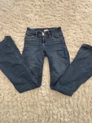 Blå bootcut jeans med broderade fickor - Snygga blå jeans från Nelly med bootcut passform och klassisk femficksdesign. Baksidan har broderade fickor med vit zigzag-söm som ger extra attityd. Jeansen har normal midja och är tillverkade i mjukt denim-material. Har blivit försmå för mig tyvärr.