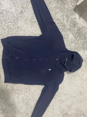 Marinblå hoodie från Polo Ralph Lauren - Säljer en marinblå hoodie från Polo Ralph Lauren i storlek M. Tröjan har huva, dragkedja framtill och två stora fickor. Klassisk Polo-logga i ljusblått på bröstet. Skön passform med custom fit och mjukt bomullsmaterial. Perfekt för chill dagar. Priset kan diskuteras