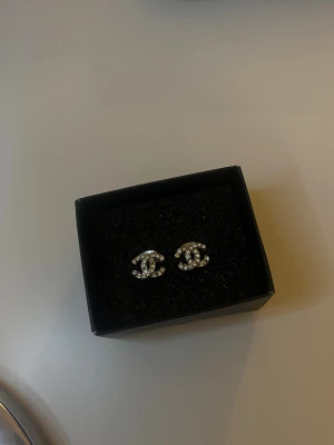 cc motiv örhängen - Snygga örhängen i klassisk CC-form, täckta med glittrande strass. De är silvriga och små, perfekta för att ge din look en lyxig touch. Kommer i original ask. Perfekt för dig som gillar statement-accessoarer och exklusiv design.