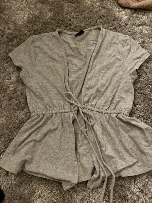 Grå omlottopp med knyt från Gina Tricot - Säljer en ljusgrå omlottopp från Gina Tricot med korta ärmar och knyt i midjan. Storlek xs🥰🥰