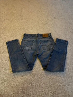 Levi's 511 blå jeans W30 L30 - Säljer ett par klassiska Levi's 511 jeans i blå denim. Modellen är slim fit med raka ben och normal midja. Jeansen har fem fickor, snygga slitningar och den ikoniska läderpatchen bak i midjan. Perfekta för dig som gillar en tidlös och stilren look. Gott skick förutom ett litet hål på vänstra bakfickan (bild 5)