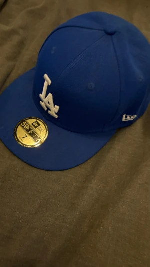 Blå LA Dodgers keps från New Era - Snygg blå 59FIFTY keps från New Era med LA logga broderad i vitt framtill. Klassisk rak skärm och broderade ventilationshål. Kepsen är i fast modell utan justering och har märkets emblem på sidan. Perfekt för dig som gillar sportig streetstyle.skriv gärna vid frågor. Pris kan diskuteras.