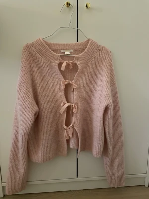 Rosa kofta med rosetter från Gina Tricot - Superfin ljusrosa stickad kofta från Gina Tricot med långa ärmar och fyra söta rosetter framtill som stängning. Koftan är mjuk och har en lite loose passform, perfekt för lager på lager under höst och vinter.