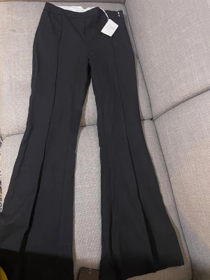 Svarta flare byxor Carin Wester stl 38 - Snygga svarta flare byxor från Carin Wester i storlek 38. Byxorna har en klassisk utsvängd passform och är tillverkade i en mix av viskos, bomull och elastan för en skön känsla och bra stretch. Perfekta för dig som gillar stilrena och trendiga byxor.