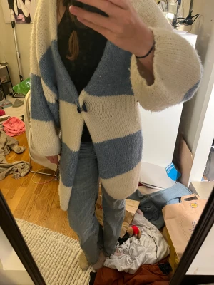 Randig stickad kofta från Lindex - Mysig och oversized stickad kofta från Lindex i storlek XS/S. Koftan har breda horisontella ränder i ljusblått och vitt, långärmad och med en enkel knapp framtill. Perfekt för lager-på-lager och chill stil.