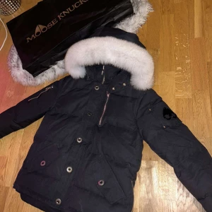 Moose Knuckles dunjacka - Säker en svart parkjacka från Moose knuckles med vit päls på huvan. Svart  Moose Knuckles logga. Storlek S. Perfekt för kalla vinter dagar.endast för 2999kr.