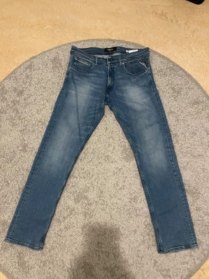 Replay blå jeans med raka ben - Snygga blå jeans från Replay med klassisk femficksdesign och raka ben. Jeansen har en diskret tvättad look och detaljer som Replay-logga på bakfickan och läderpatch i midjan. Perfekt passform och stilren look för dig som gillar tidlösa jeans.