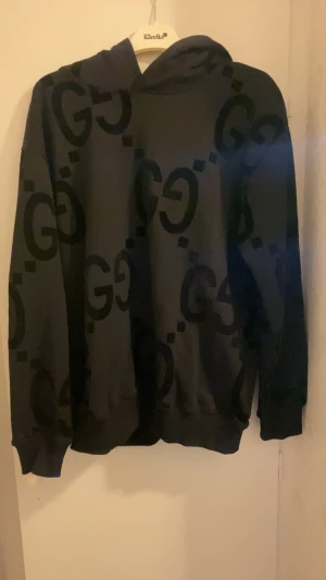 Gucci hoodie - Säljer en svart hoodie från Gucci med stort GG-mönster över hela tröjan. Hoodien har huva, långa ärmar och ribbade muddar vid ärmslut och nederkant. Perfekt för dig som gillar streetwear och vill sticka ut med en lyxig look.