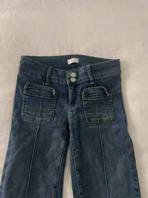 Blå jeans med fickor från Nelly - Snygga blå jeans från Nelly med två stora framfickor och dubbla silverknappar i midjan. Jeansen är bootcut! 