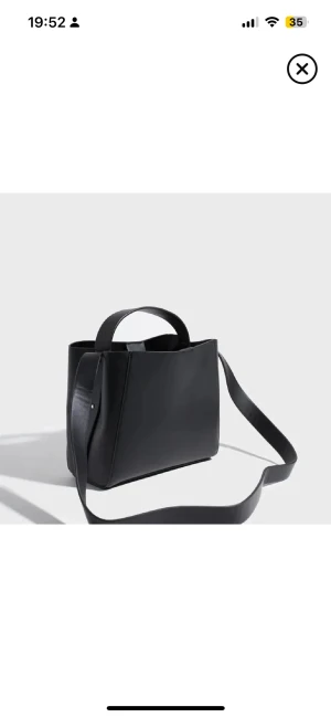 Svart axelväska i skinn - Stilren svart axelväska med minimalistisk design och bred axelrem. Väskan har både handtag och axelrem, vilket gör den enkel att bära på olika sätt. Tillverkad i slätt skinn och passar perfekt till en modern och clean look.